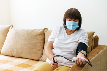 An elderly woman wearing mask measures her blood pressure with an electronic tonometer. Hypertension is risk group for the coronavirus covid-19. High blood pressure in the elderly. Elderly health - Powered by Adobe