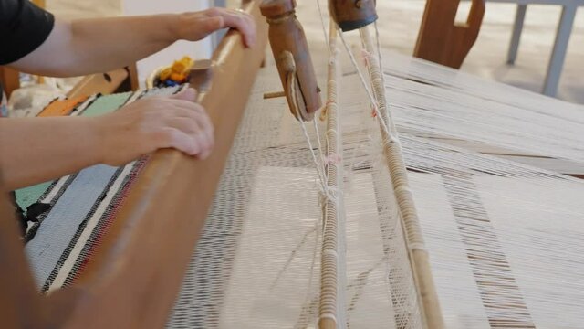 Close-up of a traditional loom as a woman waves a rug.