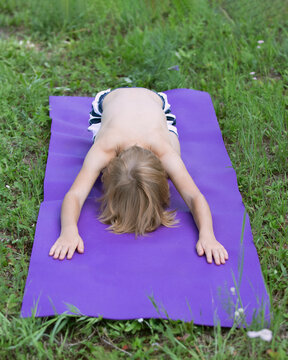 Little caucasian child does yoga, hare position in park outdoor. Shashankasana kids Yoga