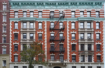 Old fashioned Manhattan apartment building facade with ornate roof cornice and external fire escape ladders - obrazy, fototapety, plakaty