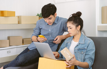 Portrait two Asian entrepreneur working together for SME small business owner. Young couple checking order from online shopping store in laptop, smartphone prepare parcel delivery in sme supply chain.