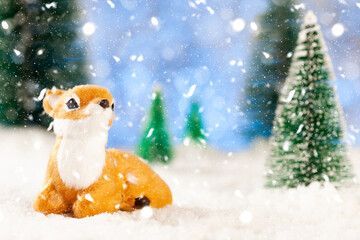 little toy deer sitting in the snow in the forest, greeting card, copy space