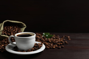 Cup of aromatic coffee and beans on wooden table. Space for text