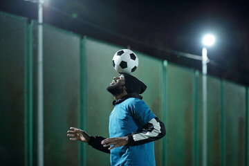 Young professional soccer player with ball on his forehead practicing difficult exercise before match or game