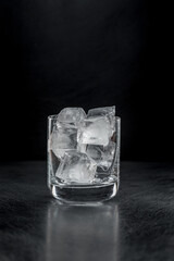 A rock glass with ice on a black background in the backlight.