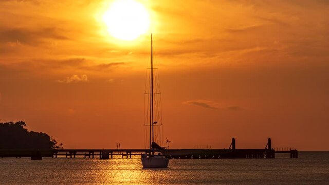 An anchored sailboat drifts from side to side as the sun sets beyond the ocean in a tropical paradise - sunset time lapse