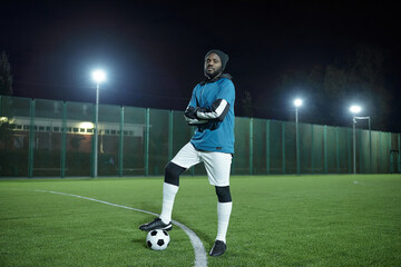 Young successful football player or trainer standing on large field at stadium during training at night
