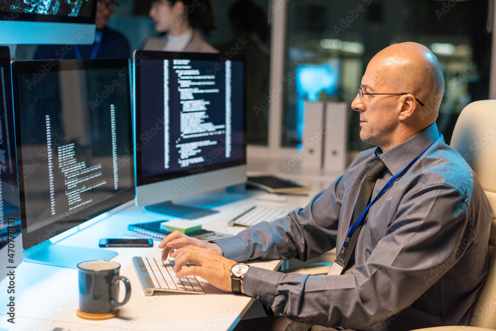 Poster Serious elegant businessman typing and looking at coded data on computer screen while decoding it in office environment