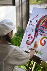 Rear view of girl painting picture on easel in art class.