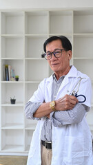 Portrait of mature doctor in white uniform standing with crossed arms in hospital.