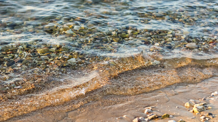 Background of sandy, stones and flowing waves on the sea beach. Summer holidays and coastal nature concept