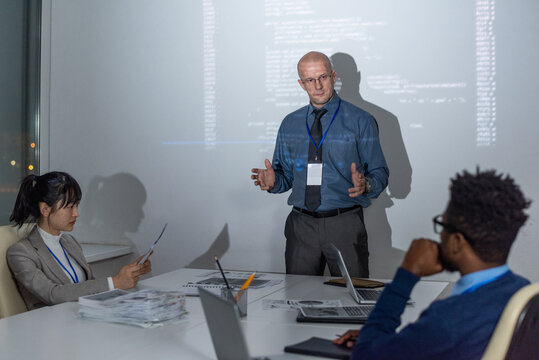 Confident mature coach or it-engineer making presentation to young intercultural subordinates or colleagues