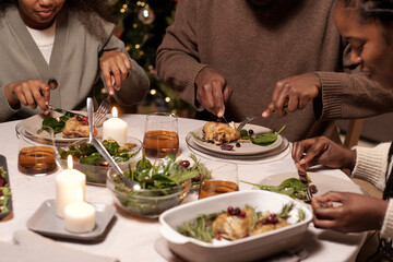 Hands of family members cutting appetizing meat on their plates while having festive dinner on Christmas day