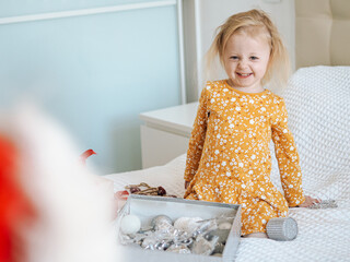 Funny blond toddler girl in yellow dress having fun in bedroom, christmas moments with winter...