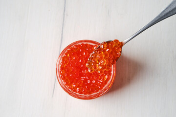 Top view of open jar with red caviar and a spoon above it