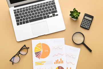 Charts with laptop, eyeglasses and magnifier on beige background