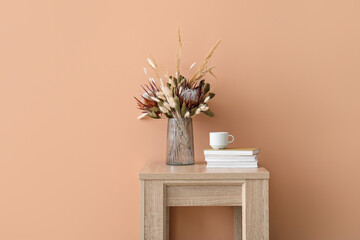 Vase with beautiful dried flowers, books and cup on table near beige wall