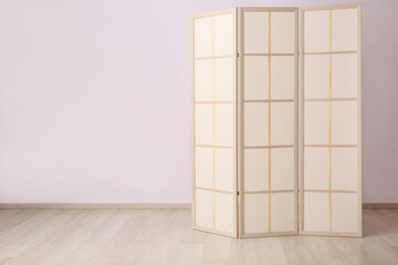 Stylish folding screen in room interior on wall background