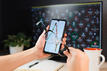 Trading, investment, business, finance and technology. Close-up of smartphone with professional candlestick chart. Businessman analyzing stock market on mobile app using glasses