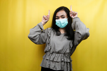 Beautiful young woman wearing a mask with hands pointing up, presenting something, isolated