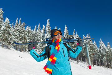 Young male skier holding ski; blue jacket; black pant; horizontal orientation - obrazy, fototapety, plakaty