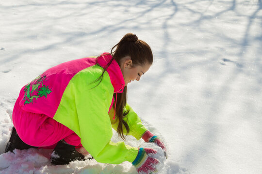 Smiling Girl Rolling A Huge Snowball In Wintertime