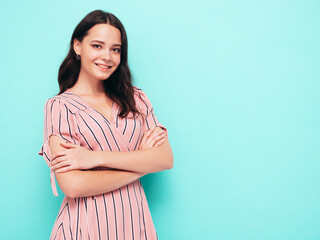Obraz premium Portrait of young beautiful smiling female in trendy summer pink dress. Sexy carefree woman posing near blue wall in studio. Positive model having fun indoors. Cheerful and happy