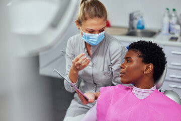 Female dentist explaining Tooth X-Rays to a african patient - obrazy, fototapety, plakaty