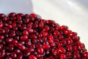The surface of dogwood jam. Ripe red berries in syrup. Cooking of homemade cornel jam. White bowl.