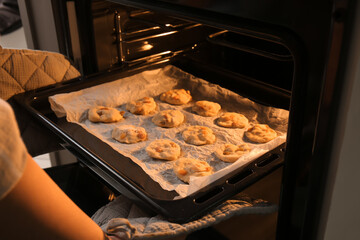 Woman putting baking tray with homemade cookies in oven