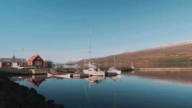Sailboats moored to small dock in Akureyri, Iceland on calm, sunny morning.