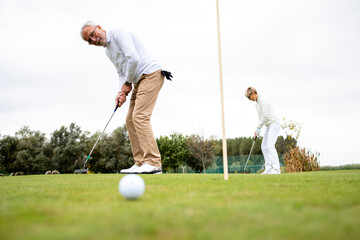 Senior active people playing gold at the golf course and enjoying free time outdoors.