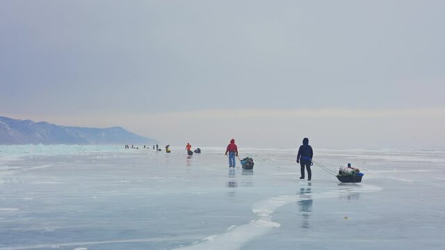 Row of tourists with equipped sledges move over frozen ice. Winter hiking trek