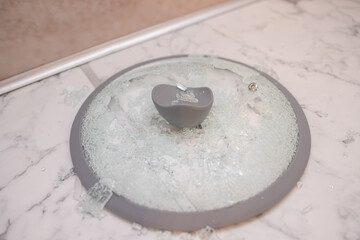 A close-up of a broken glass lid lies on a stake of tile. shards of glass shine. soft focus, top...
