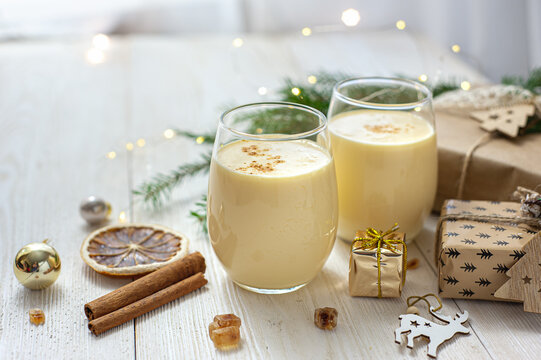 Two glasses of eggnog on a white wooden table next to the Christmas presents. Sweet egg dessert. Christmas breakfast.