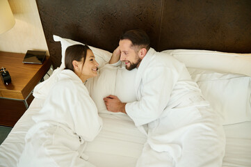 High angle view of a couple in love, newlyweds on their honeymoon. Beautiful woman lying in bed with her husband and enjoying the privacy of the weekend together at home. Family relationship