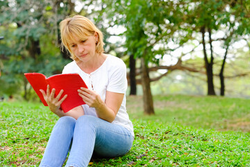 caucasian senior woman happy in park and reading a book