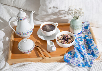 breakfast in bed on a wooden tray with a cup of coffee, tea set and oatmeal