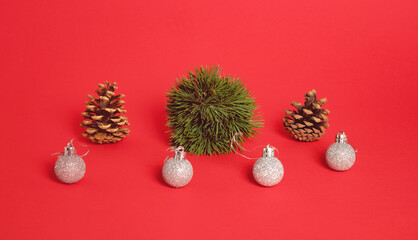 Decoration ball made of pine tree, pine cones and plastic decoration balls stand on pastel red background. Minimal horizontal composition,  Christmas and New Year abstract decorative  concept