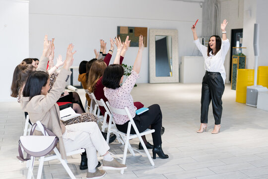 Rear view of women sitting with their hands up in training meeting. Group of female attending at seminar and performing the tasks of the speaker during Motivational sessions