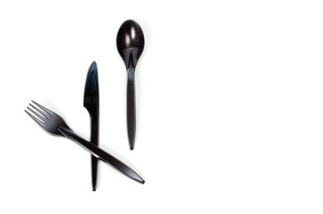 A set of plastic cutlery knife, fork and spoon in black, filmed on a white background