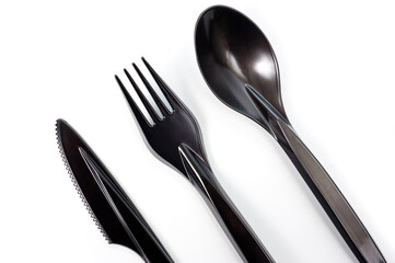 A set of plastic cutlery knife, fork and spoon in black, filmed on a white background
