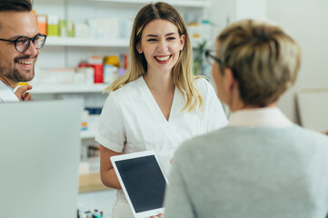 Obraz premium Two pharmacist giving prescription medications to senior female customer in a pharmacy