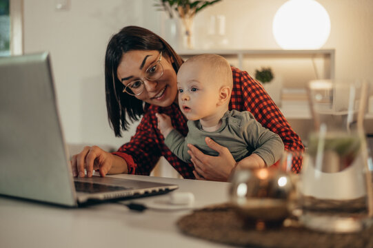 Beautiful business mom using a laptop and spending time with her baby boy at home