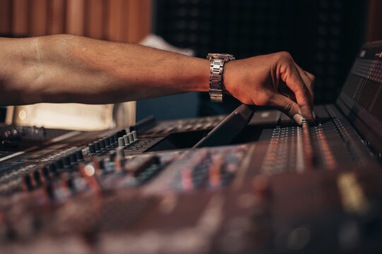 Hands of a producer working on a mixing soundboard while in his studio