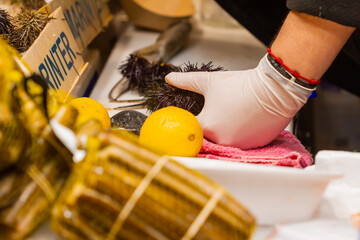 Fishmonger's store with unrecognizable woman cleaning sea urchin, selective approach at hand.