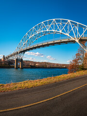 Fototapeta premium Sagamore Bridge and paved bikeways along the Cape Cod Canal. Peaceful and safe outdoor recreational park in Bourne, Massachusetts. Arching landmark metal bridge connecting Massachusetts mainland to Ca