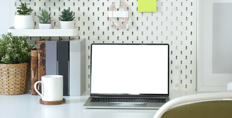 Front view computer laptop with empty display, books and potted plant on white table..