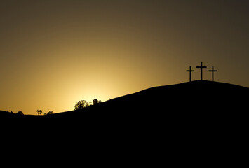 three crosses backlit on top of a mountain at sunrise with a golden sky. copy space, text space
