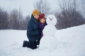 grandmother with a small granddaughter make a creative snowman and play in nature in winter. family spends time together in winter in nature